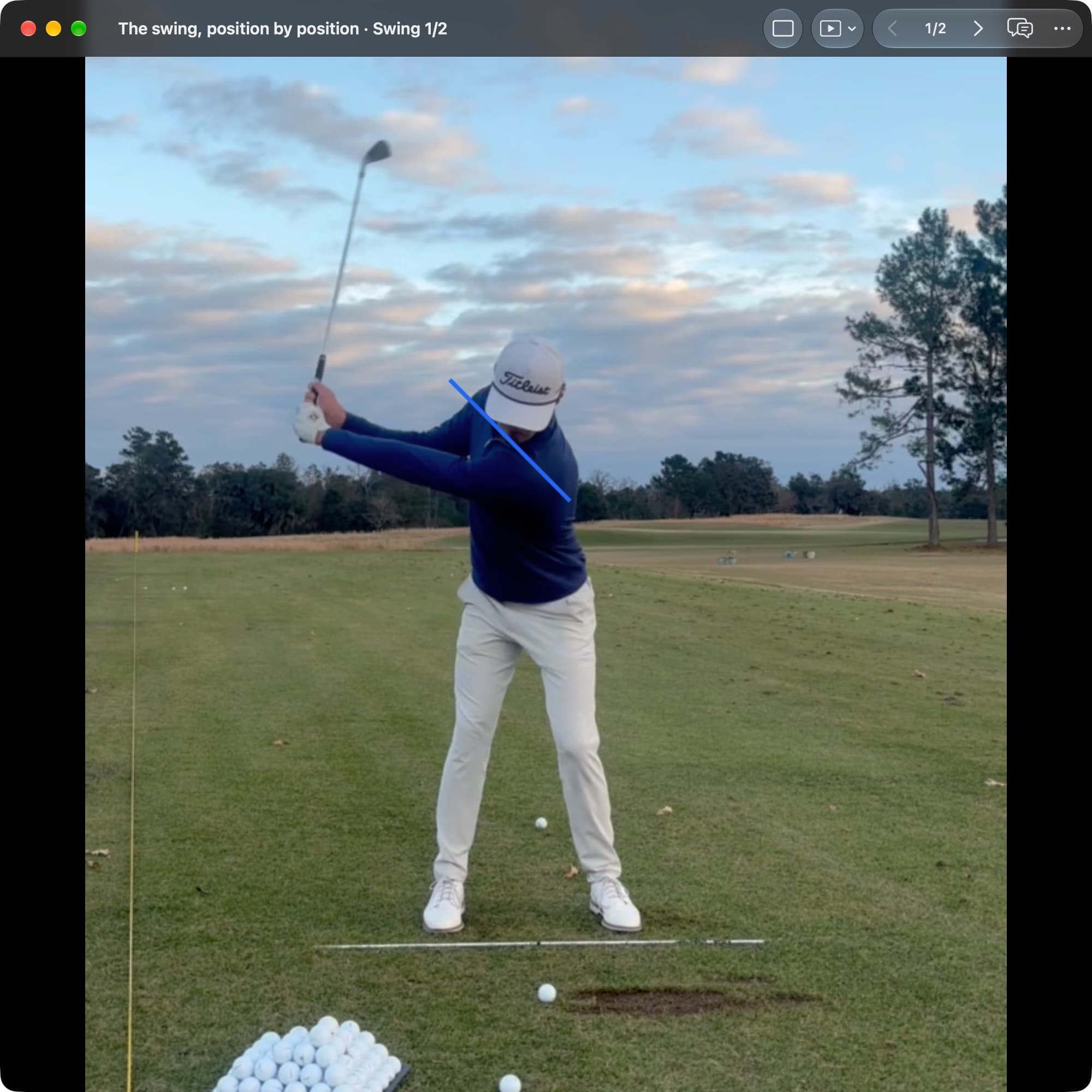 A golfer in MotionEdge Video Player, face-on on a range, in the backswing with the club pointing up. A blue line runs across the shoulders, tilted with the turn.