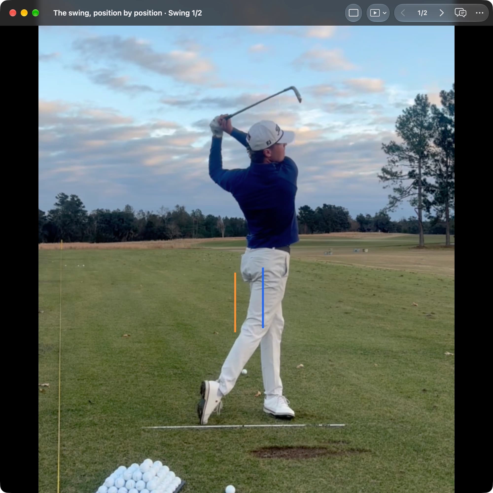 A golfer in MotionEdge Video Player, face-on on a range, at the finish with the club over the shoulder. An orange line marks the pelvis center at Address and a blue line sits over the lead foot.