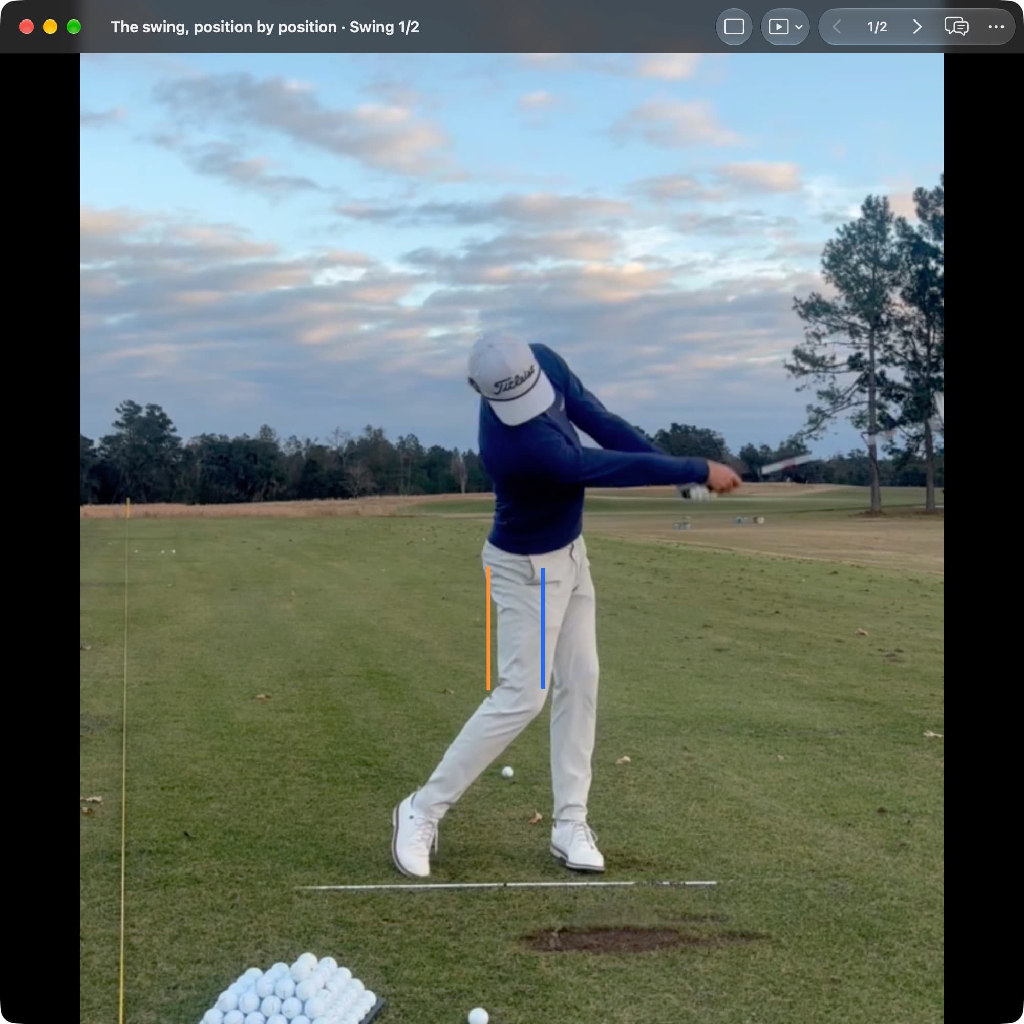 A golfer in MotionEdge Video Player, face-on on a range, in the follow-through with the arms extended toward the target. An orange line marks the pelvis center at Address and a blue line sits well toward the target.
