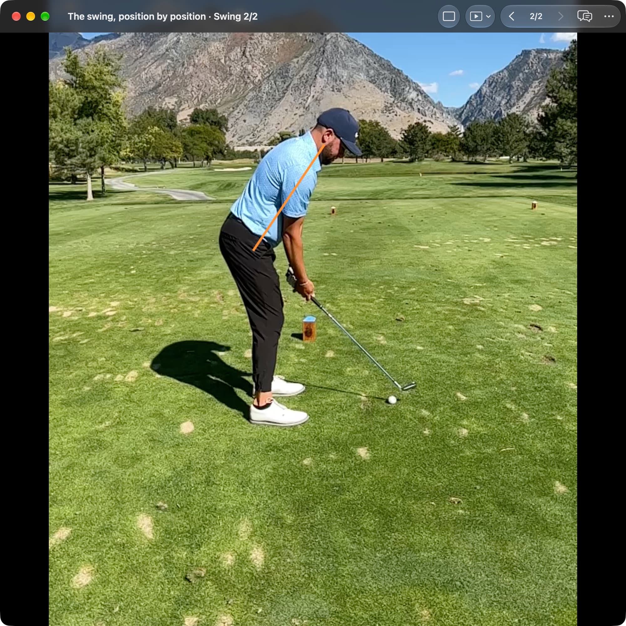 A golfer at Address in MotionEdge Video Player, down-the-line on a course. An orange line runs from the hips toward the shoulders along the forward-bent torso, and the arms hang toward the club resting behind the ball.