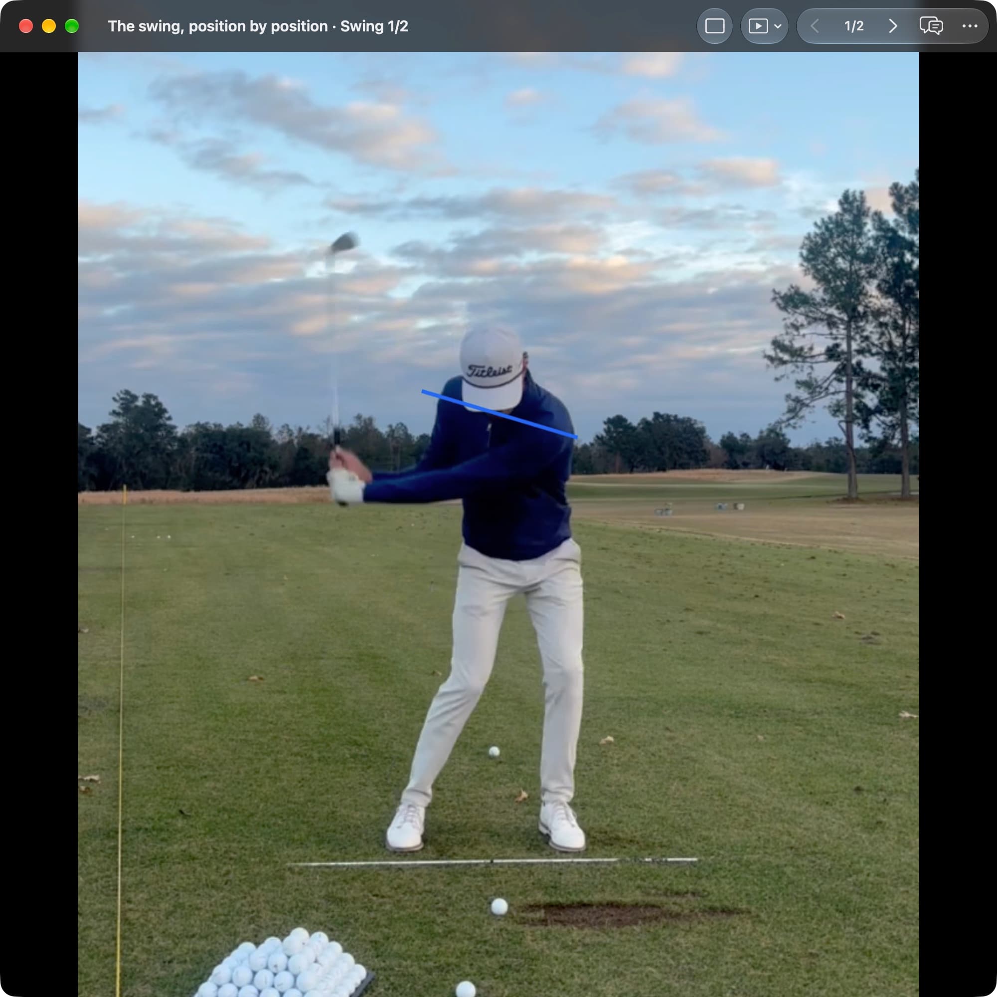A golfer in MotionEdge Video Player, face-on on a range, in the downswing with the hands above the waist. A blue line runs across the shoulders, closer to level than at the top.