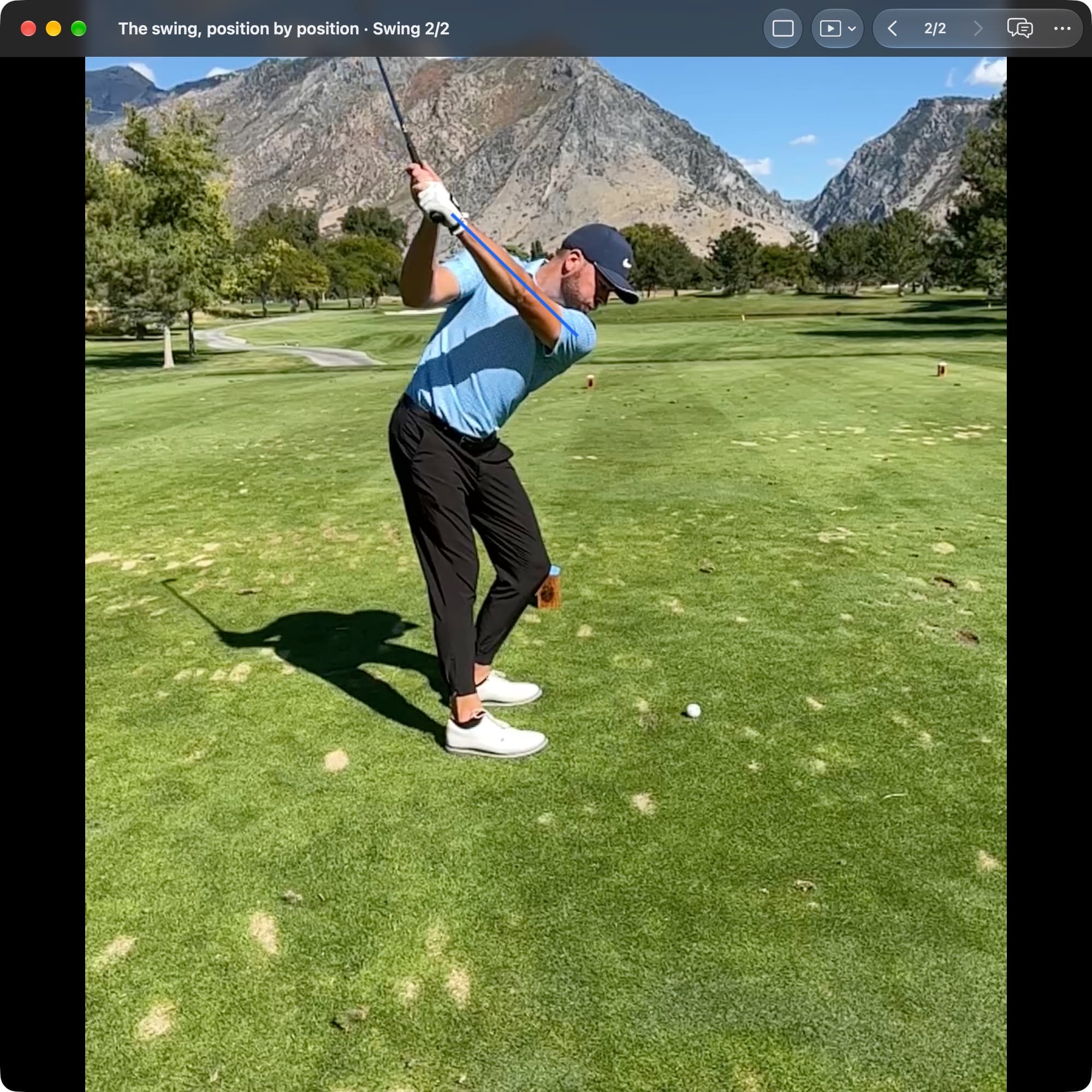 A golfer in MotionEdge Video Player, down-the-line on a course, near the top. The blue lead-arm line rises toward the hands, with the club pointing up and farther around the body than in the earlier frame.