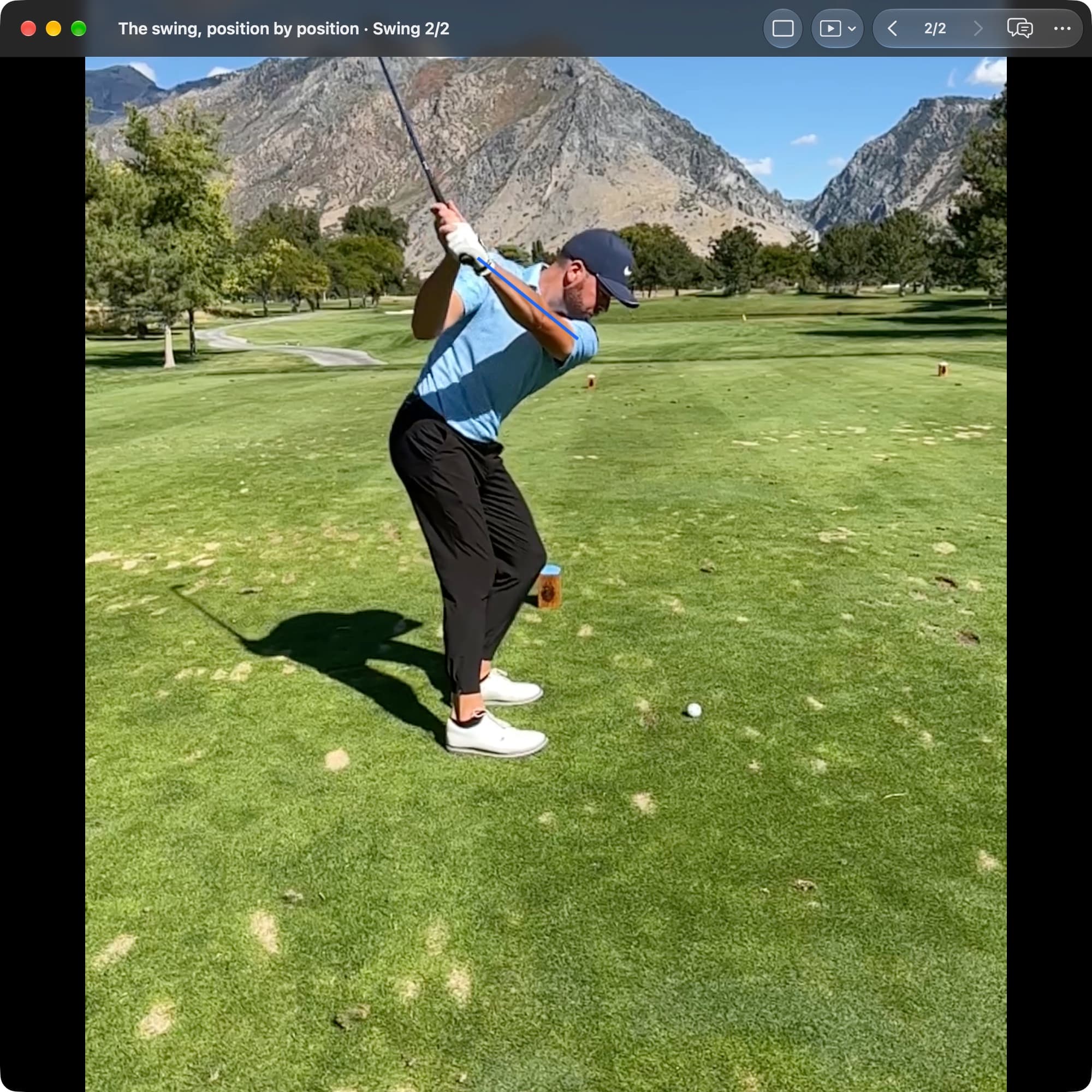 A golfer in MotionEdge Video Player, down-the-line on a course, at the change of direction with the club above the head. A blue line follows the lead arm from shoulder to hands.