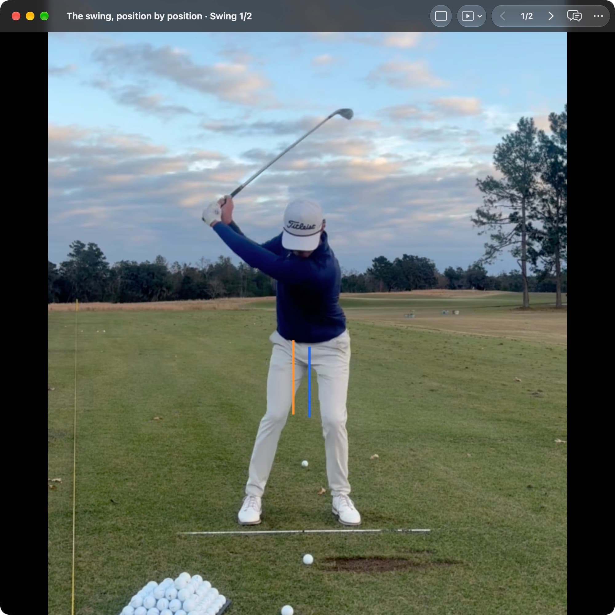 A golfer in MotionEdge Video Player, face-on on a range, near the top with the club behind the head. An orange line marks the pelvis center at Address and a blue line sits slightly toward the target.